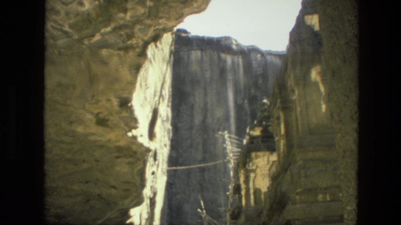 1974 India home-movie frame looking through a rocky opening toward carved temple architecture in bright sun and deep shadow.