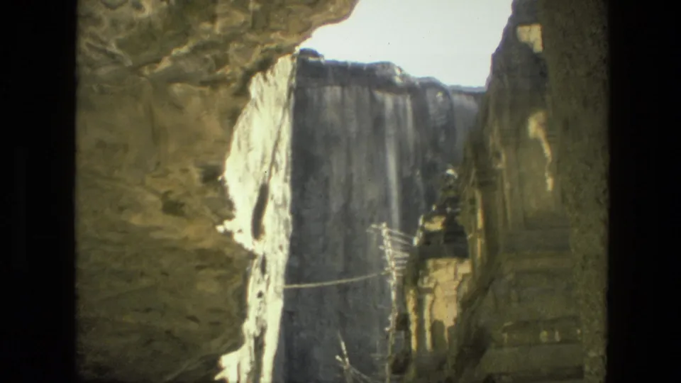 1974 India home-movie frame looking through a rocky opening toward carved temple architecture in bright sun and deep shadow.
