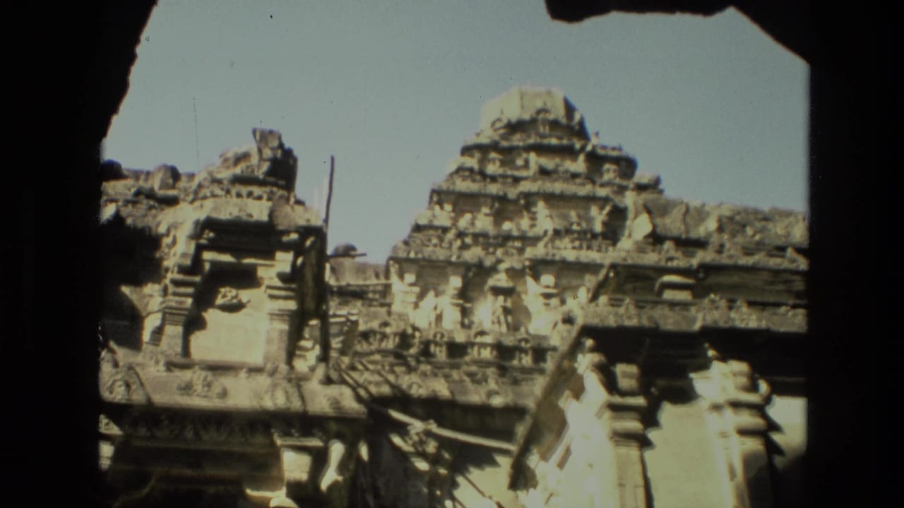 Handheld 1974 India temple footage frames layered stone carvings and a tower through a dark passage opening.