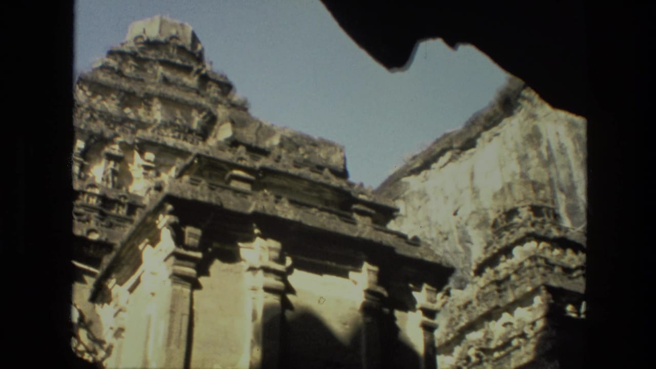 Sunlit carved temple wall and pillars seen through a dark opening.