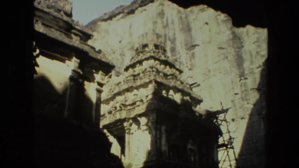 1974 India 8mm frame showing a carved temple tower, weathered wall, visible scaffolding, and deep shadow along the left edge.
