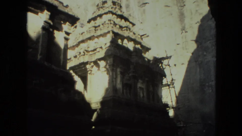 1974 India home-movie frame of sunlit carved temple architecture, shadowed pillars, pale wall surfaces, and scaffolding along one side.