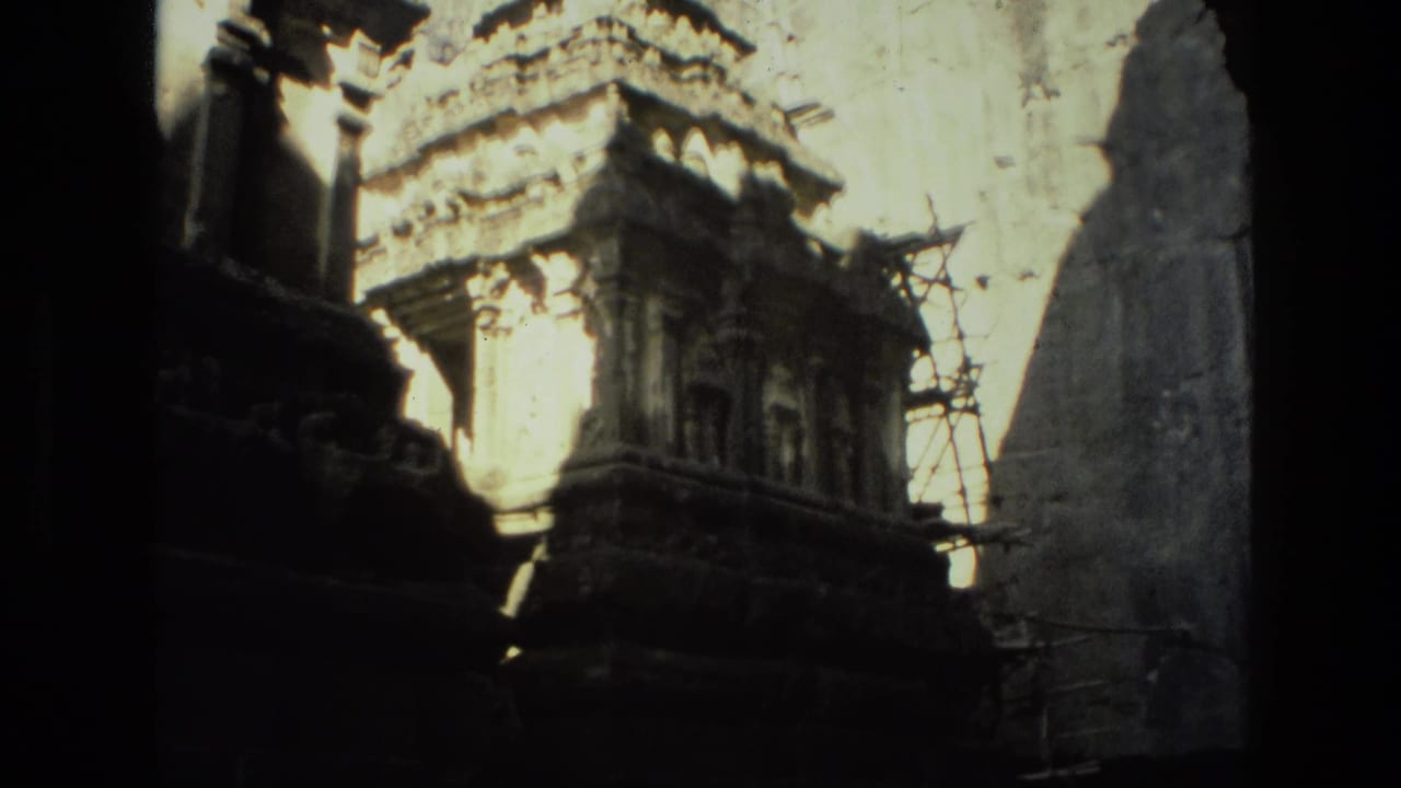 Dark 8mm frame of carved stone temple structures with scaffolding and deep shadow.