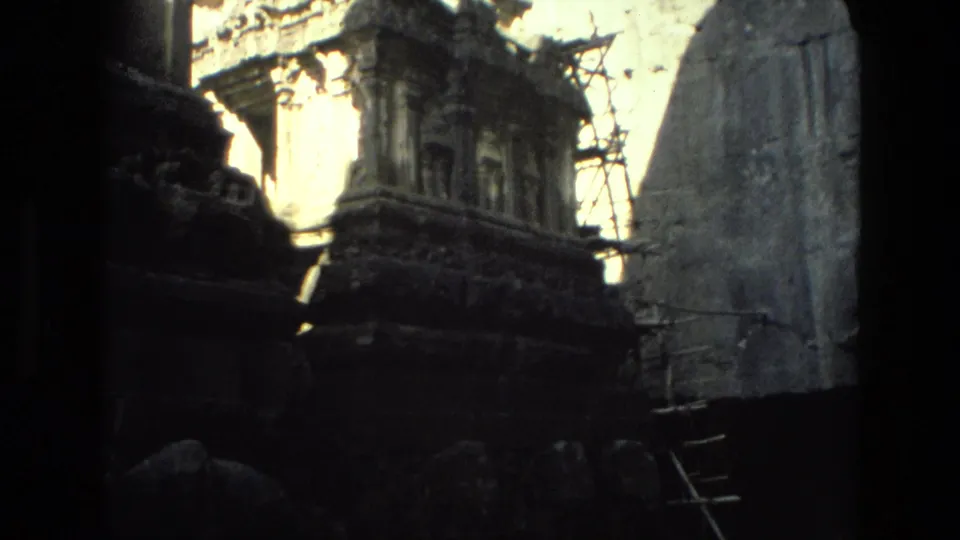 A visitor-shot 8mm view in India shows a carved temple structure, surrounding stonework, scaffolding, and dense shadow.