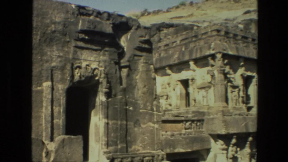 1974 India 8mm frame showing a carved rock-cut temple entrance with sculpted figures, dark doorway, and weathered stone surface.