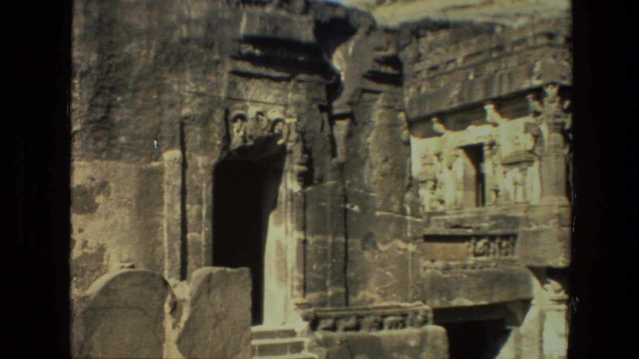 Carved stone temple facade with doorway, relief figures, and rock wall.