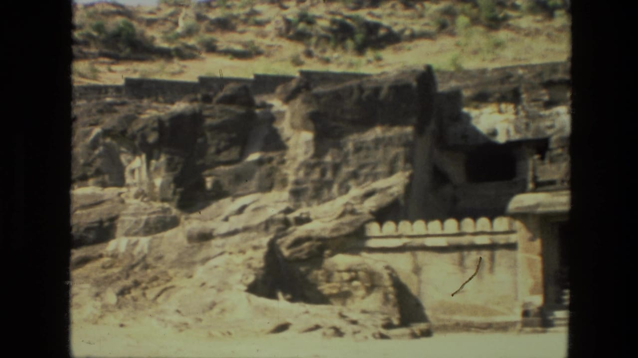 Rock-cut cave temple facade and low wall in a dry hillside.