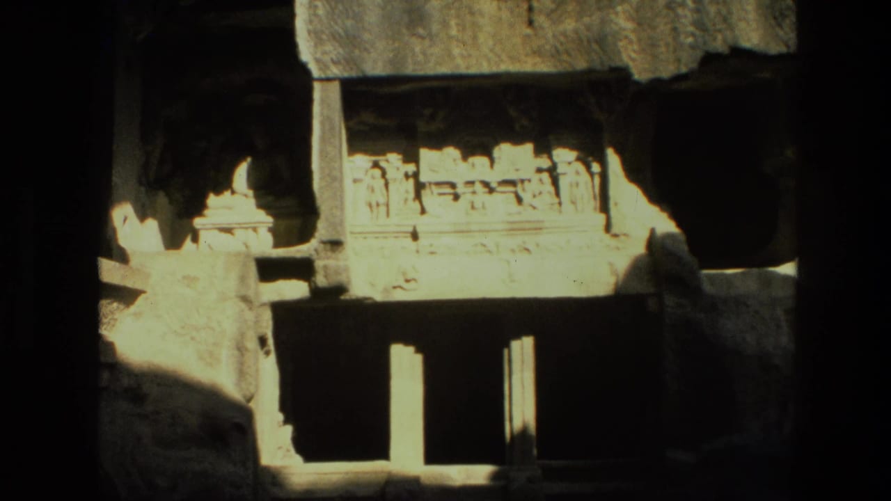 Carved stone temple facade under a rough rock overhang with dark openings below.