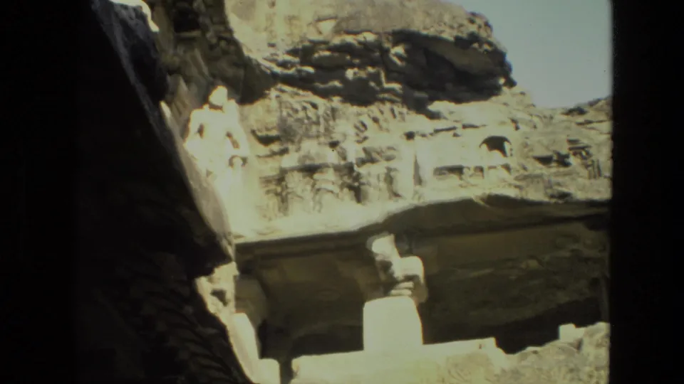 1974 India frame showing an angled rock-cut architectural facade with carved recesses, bright sky, and lower stone supports.