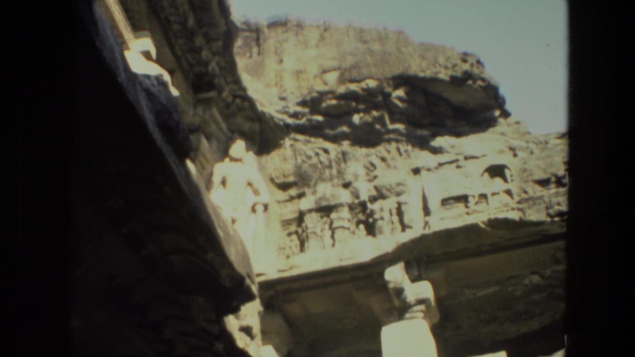 Bright cave opening with rocky exterior and carved stone forms at the edge of a temple interior.
