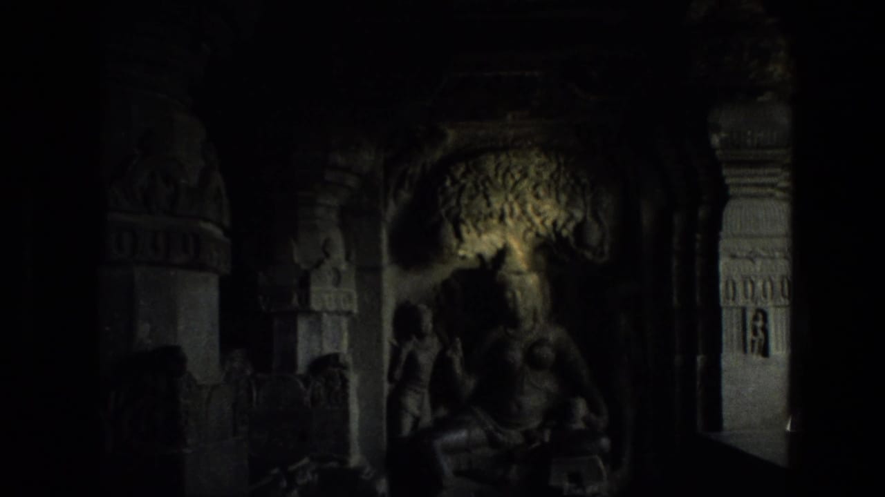 Dim carved chamber with a seated religious statue and ornate stone pillars.