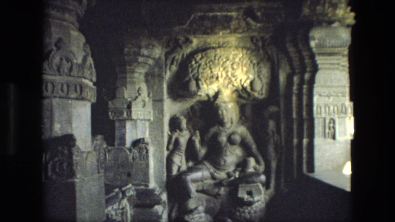 Dim stone chamber with carved seated figure, pillars, relief details, and deep shadows.