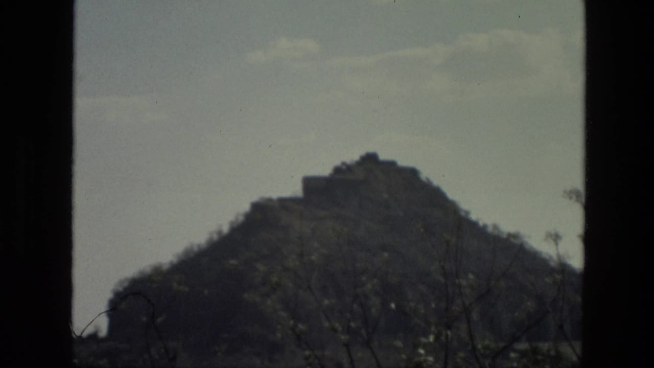 Distant brown hill with a small structure near the top, seen through dark frame edges.