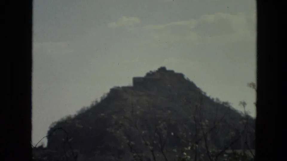 1974 India 8mm frame showing a distant brown hill and small hilltop structure viewed through dark foreground edges.