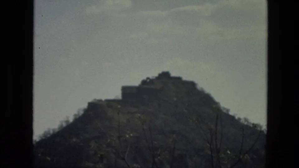 1974 India 8mm frame of a brown hill and small structure on the crest, with dark foreground framing and pale sky.