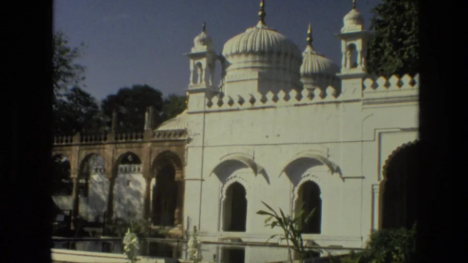 1974 India 8mm frame showing a white domed building with arched openings, garden planting, and trees.