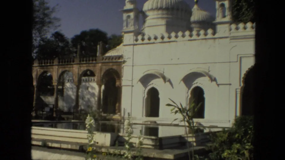 1974 India 8mm frame of white domed architecture with arched windows, garden planting, and dark foreground framing.