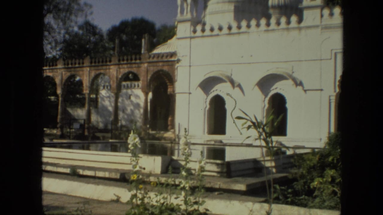 White palace facade with arched colonnade, courtyard pool, plants, and trees.
