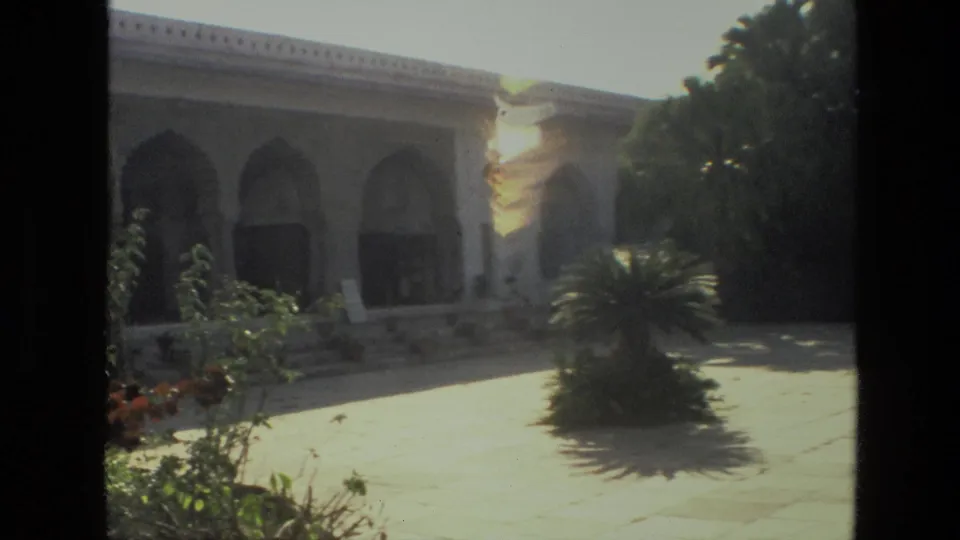 1974 India 8mm frame showing an arched stone structure, planted courtyard, and bright sunlit paving.