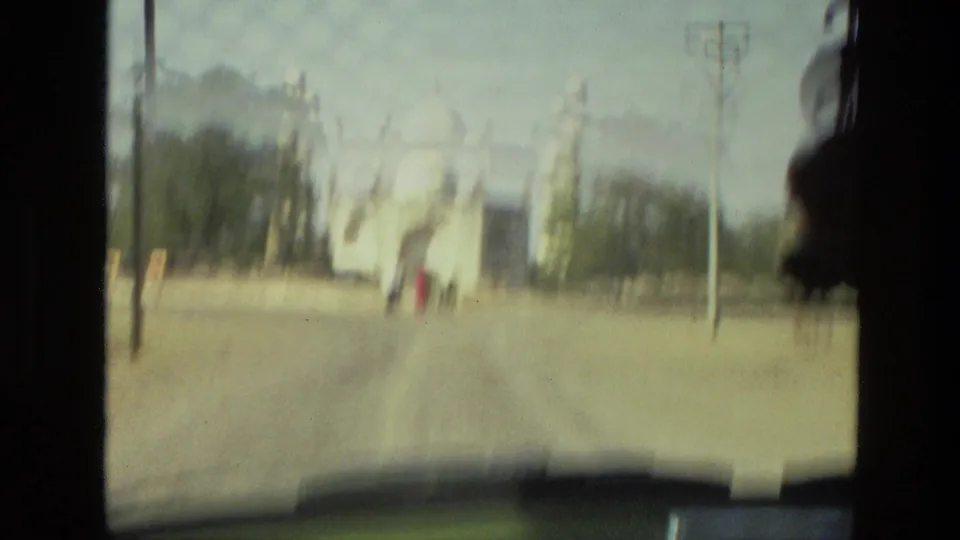 Soft 1974 India vehicle-window view approaching a pale domed historic structure with visitors ahead.