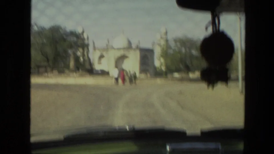 1974 India 8mm frame from inside a vehicle, with visitors walking toward a white mausoleum-like building.