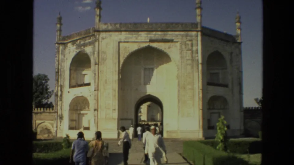 1974 India frame showing visitors approaching a large white arched mausoleum-like gateway amid formal lawns.