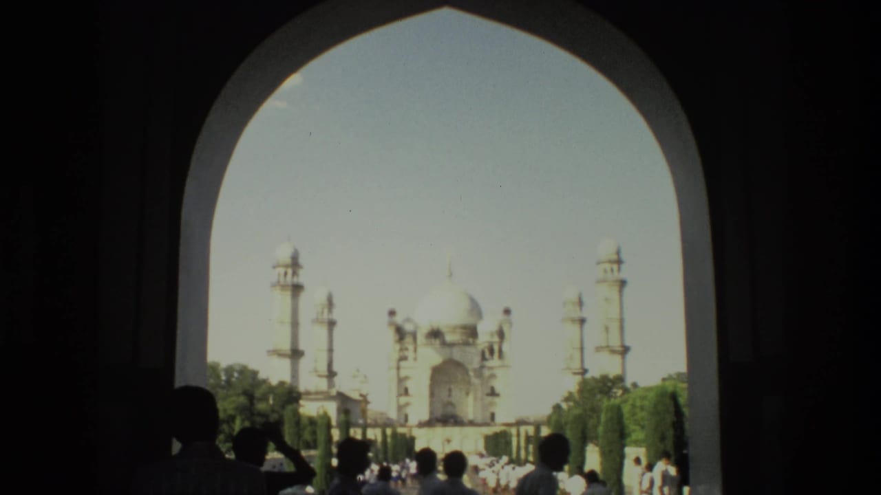 Taj Mahal seen through a large dark arch with tourists silhouetted in the foreground.