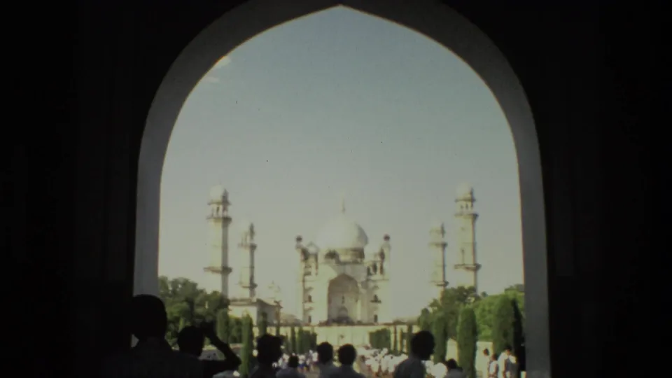 1974 8mm view of the Taj Mahal framed by a shaded arch, with visitors silhouetted near the entrance.