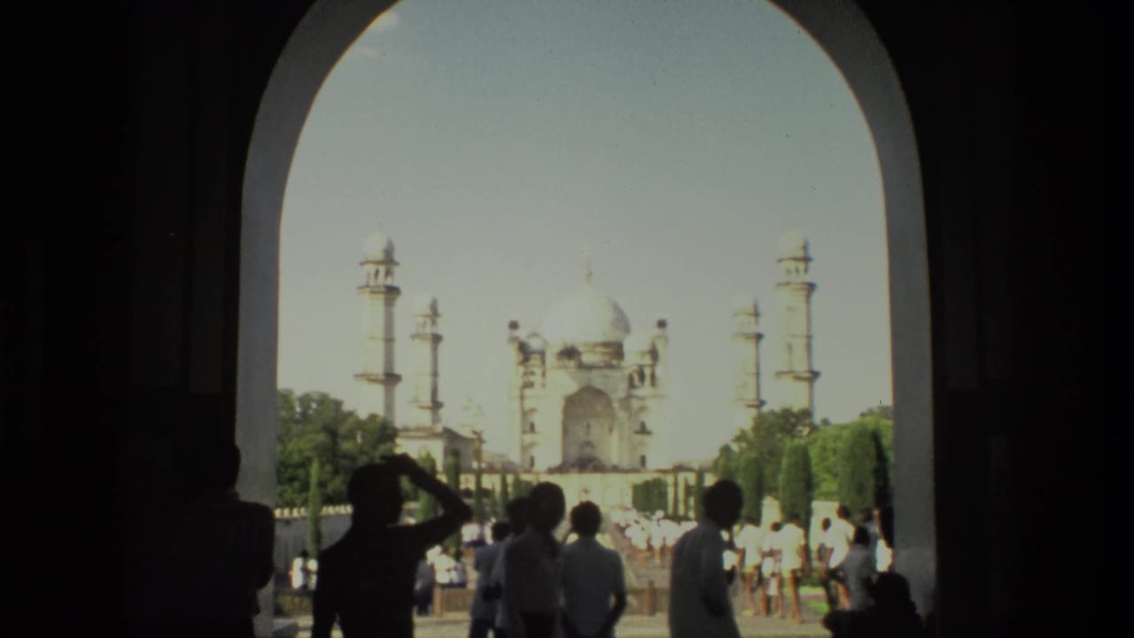 Tourists stand in shadow beneath an arch while the Taj Mahal appears beyond the garden.