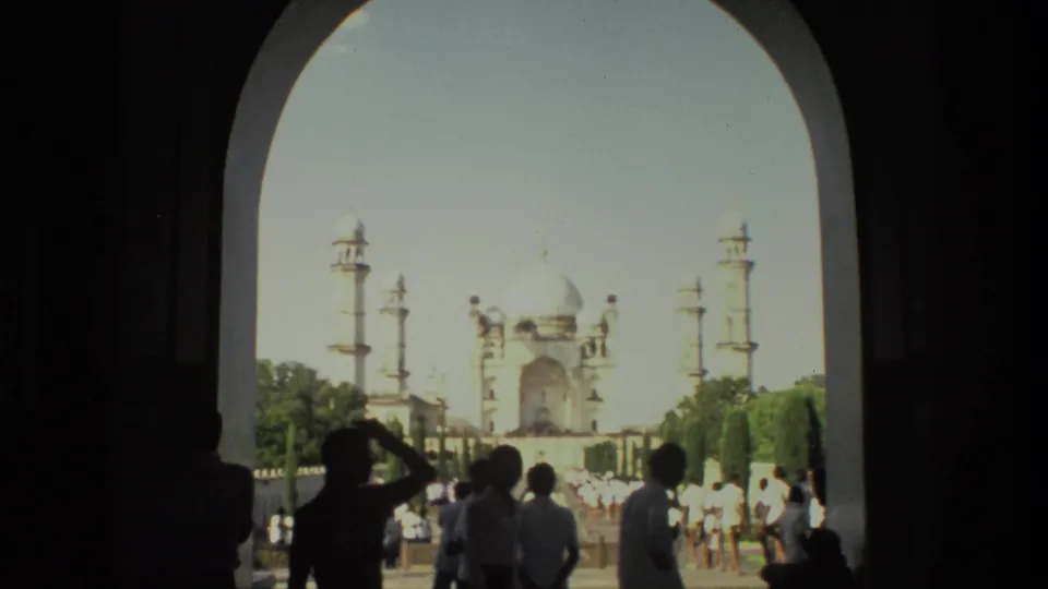 Visitors in silhouette look toward the Taj Mahal from a shaded archway in this 1974 India travel frame.