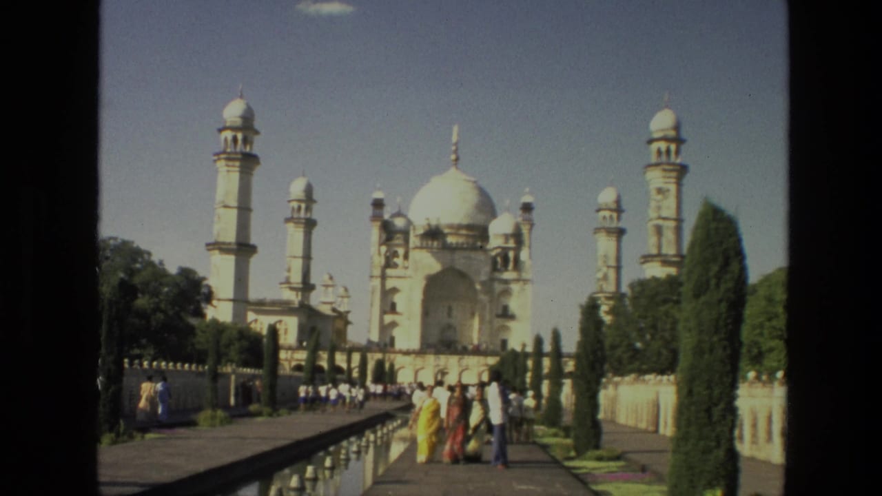 White domed monument with minarets, reflecting pool, walkways, trees, and tourists.