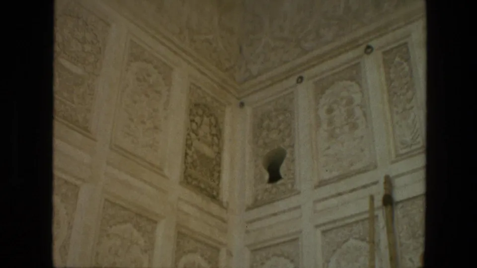 1974 India 8mm frame looking up at carved pale wall panels and ceiling detail inside or near the monument, with an arched niche visible.