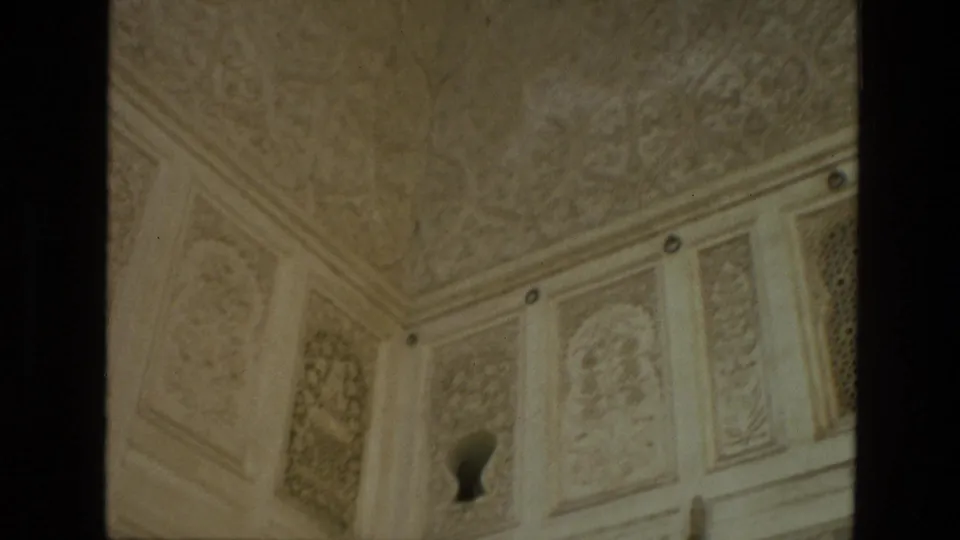 1974 India 8mm frame showing carved architectural panels, a decorated ceiling corner, and a small keyhole-shaped opening in a pale wall.
