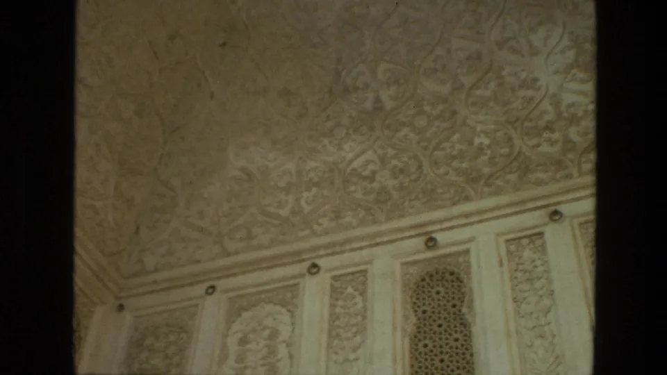 1974 India 8mm frame of ornate carved ceiling detail, vertical decorative wall panels, and an arched lattice screen in a monumental building.
