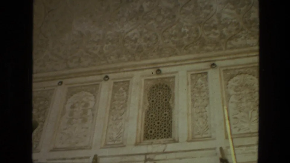 1974 India 8mm frame showing angled carved wall panels, an arched lattice screen, ceiling relief, and dark borders from the film scan.