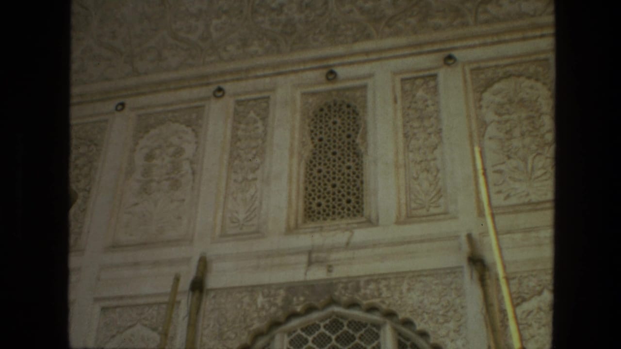 Pale carved wall with small lattice window panels and a partial arched opening below.