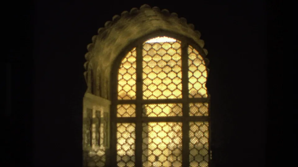 1974 India home-movie frame of a warmly illuminated arched temple lattice window with a scalloped surround and dark adjacent framing.