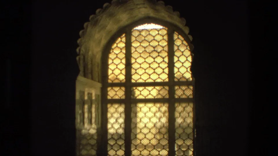 1974 India 8mm frame of a luminous arched lattice window set in a dark interior wall.