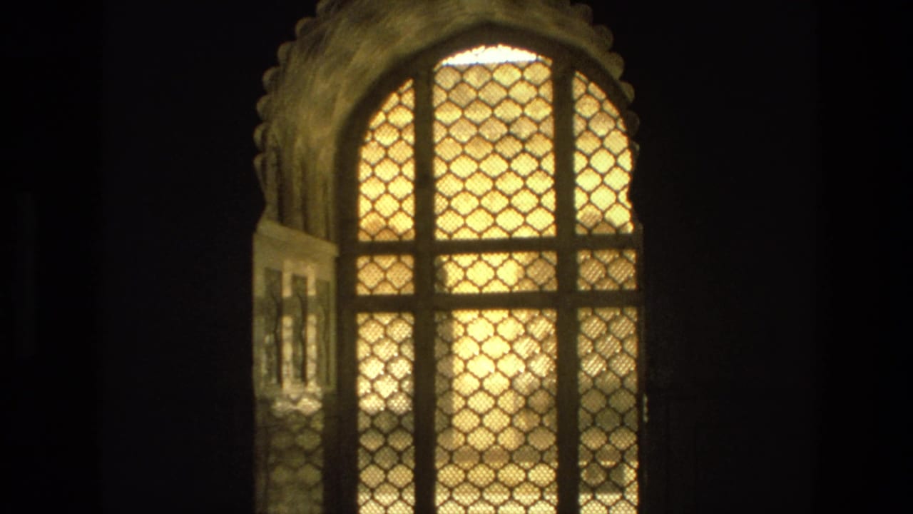 Arched lattice window with warm light and surrounding darkness.