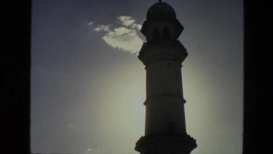 Minaret-like tower silhouetted through a window frame in 1974 India archival 8mm footage.