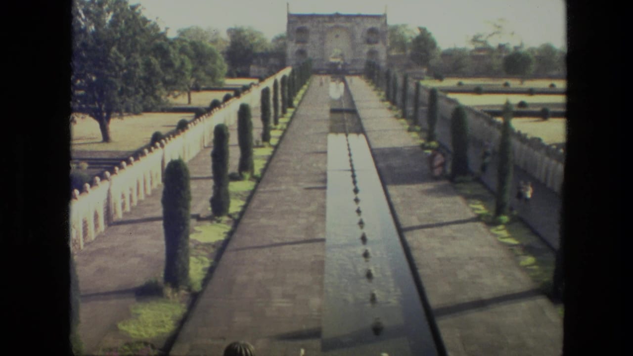 Formal garden walkway with reflecting pool leading toward an arched gateway.