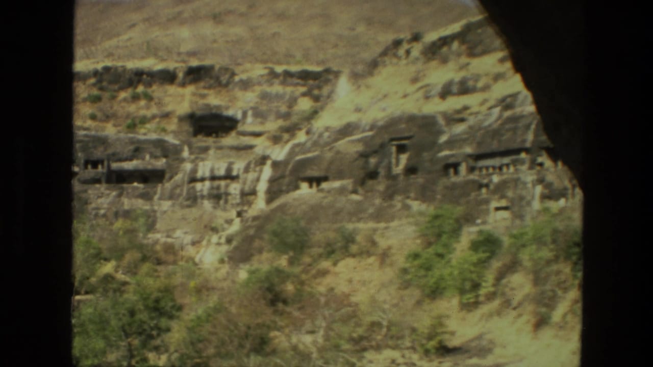 Rocky hillside with cave openings and carved structures partly framed by dark foreground edges.