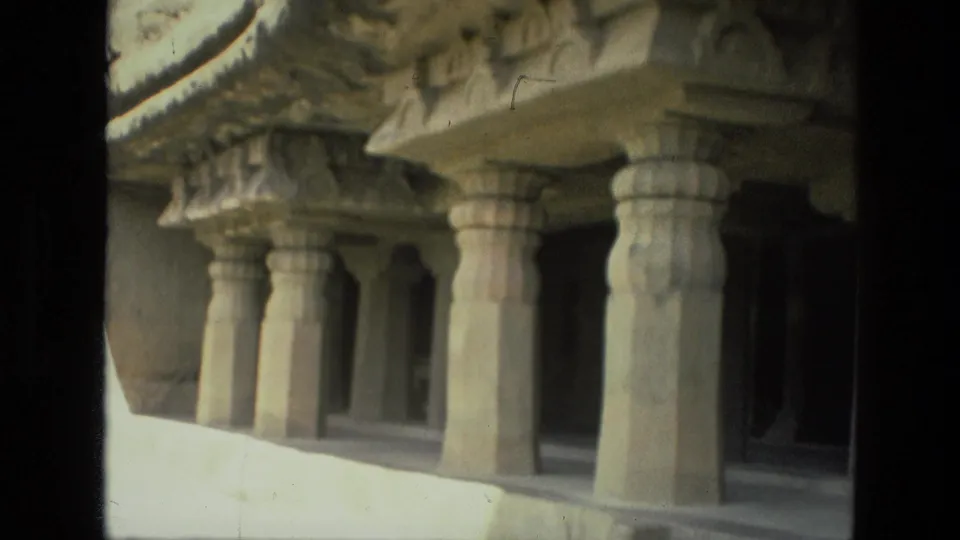 1974 India 8mm frame showing carved stone pillars supporting a rock-cut cave facade with deep shadowed entryways.