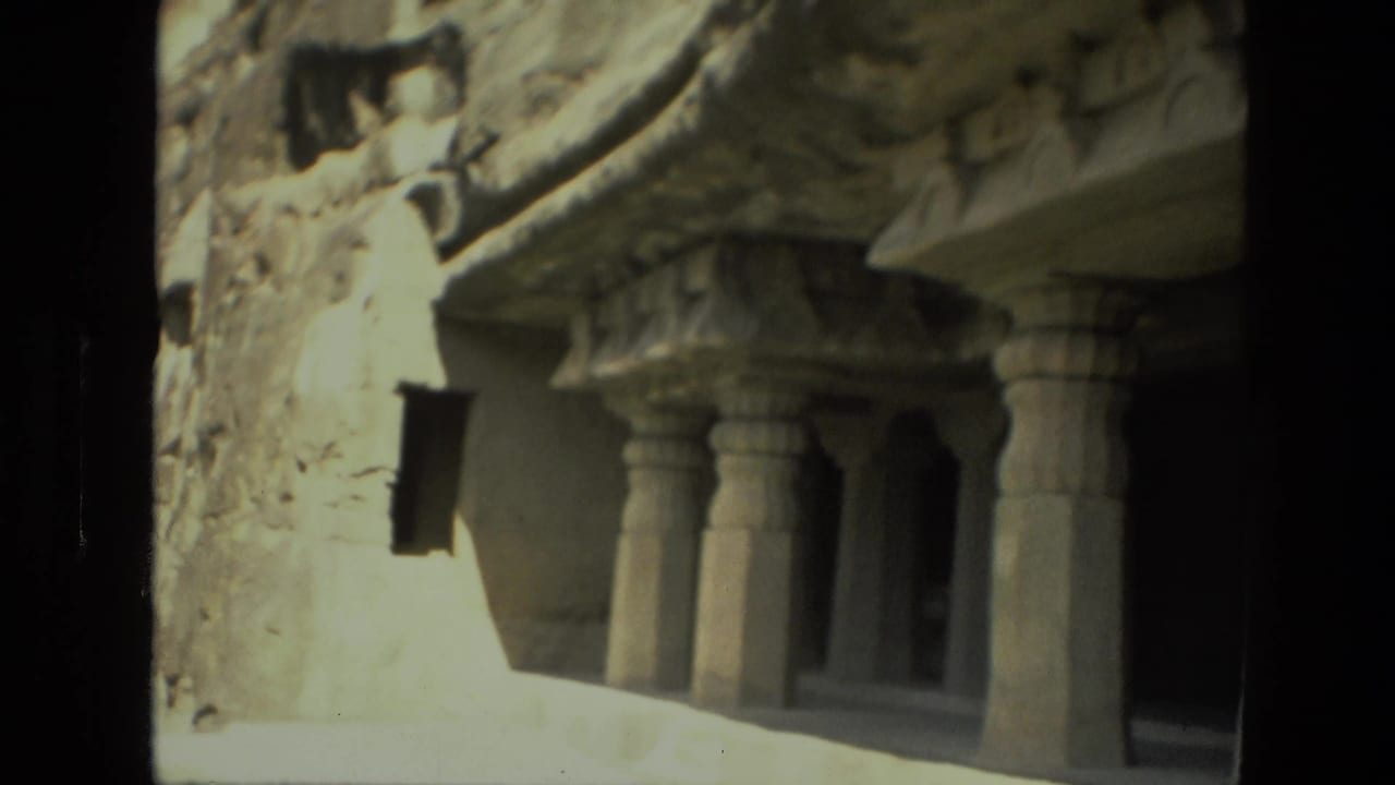 Rock-cut temple facade with carved pillars and a dark recessed entrance.