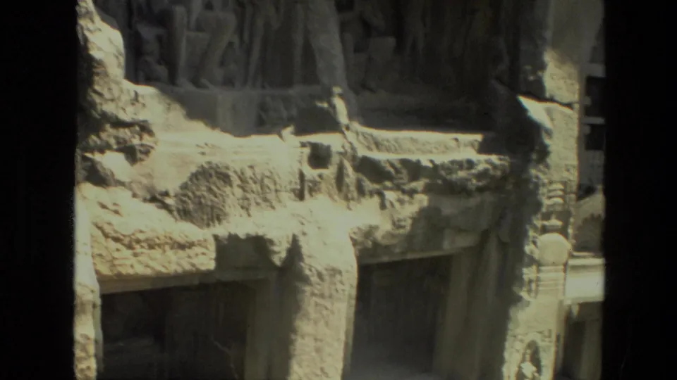 Faded 8mm frame of Indian rock-cut temple carvings, with relief figures above rough stone and a dark lower doorway.