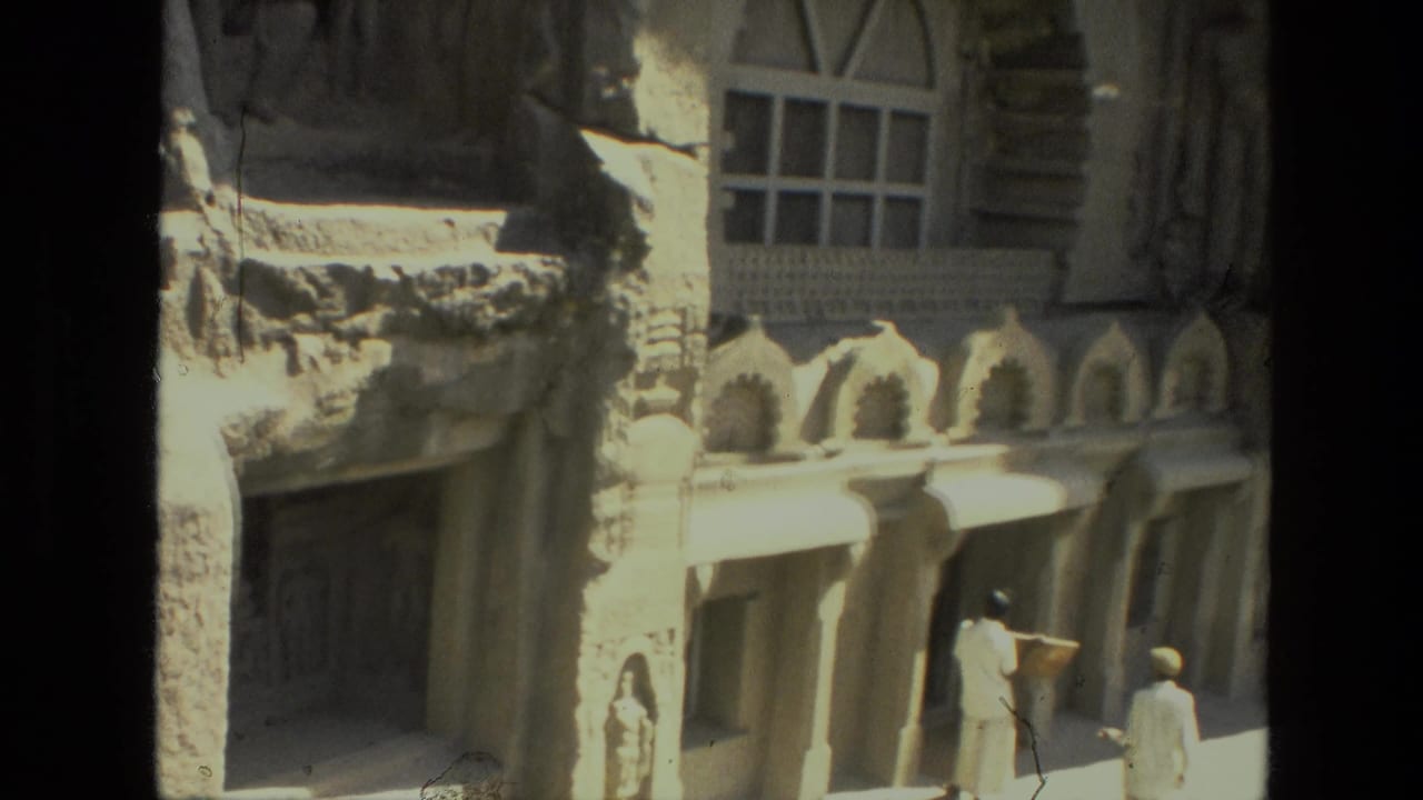 Carved building facade with arched windows and small visitors near a shaded entrance.