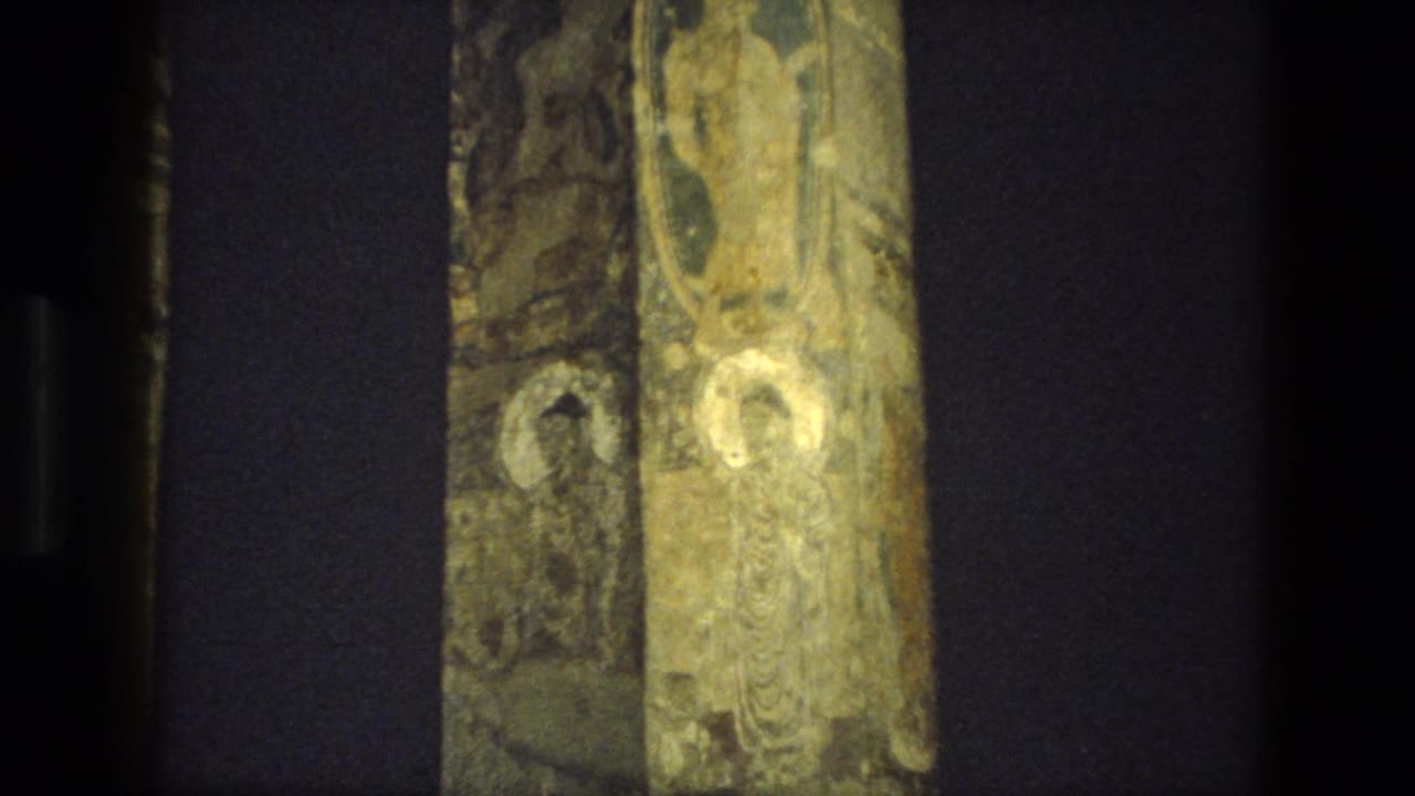 A handheld 8mm view of painted stone columns and shadowed recesses inside an Indian cave-temple setting.