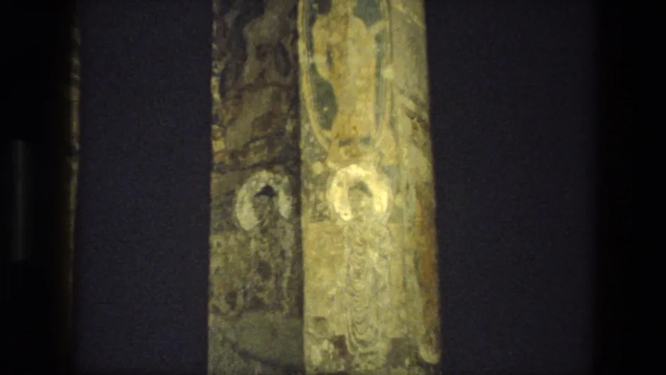 A handheld 8mm view of painted stone columns and shadowed recesses inside an Indian cave-temple setting.