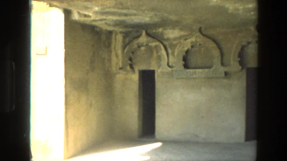 1974 India 8mm frame showing arched stone niches, dark doorways and a bright side opening in a cave-temple interior.