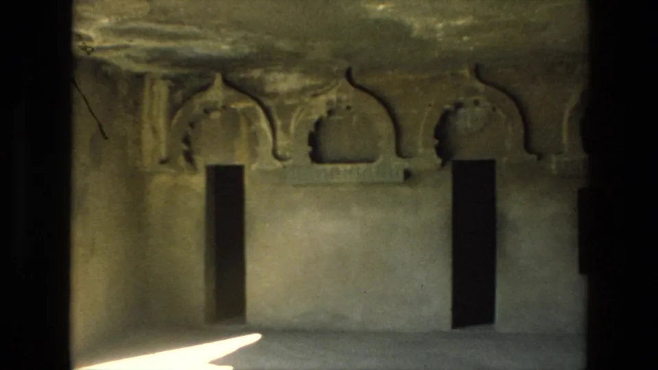 A cave-temple wall in India, filmed on 8mm in 1974, with arched niches, dark openings and weathered stone detail.